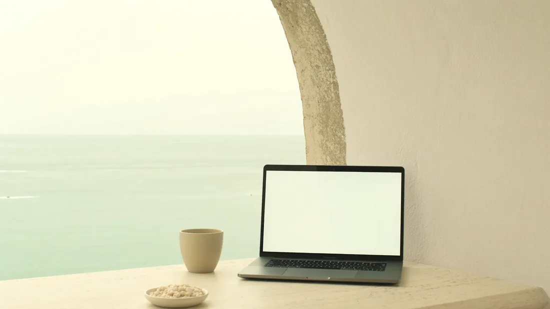 Laptop on a terrace, the view through a plaster arch onto a calm sea