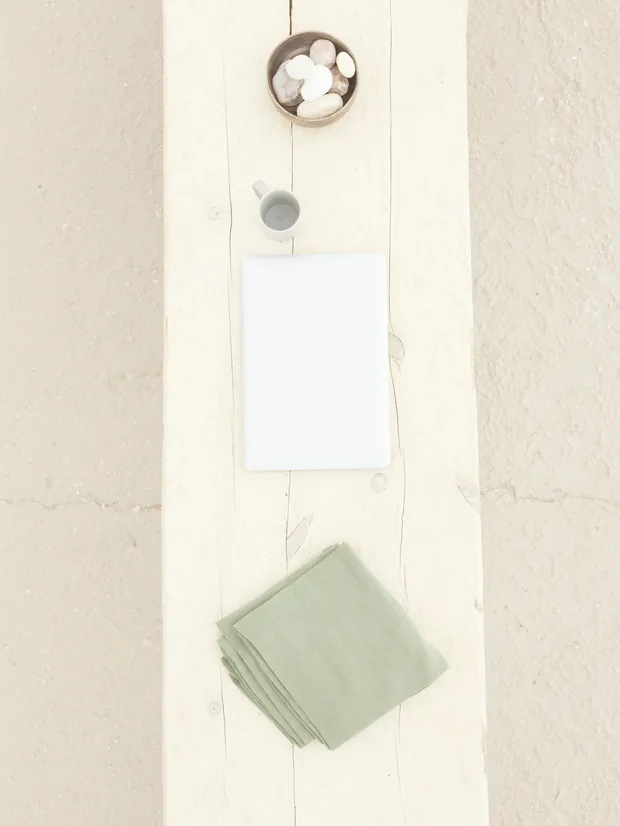 Top view of a closed laptop, a cup and a sage-green linen cloth on light wood