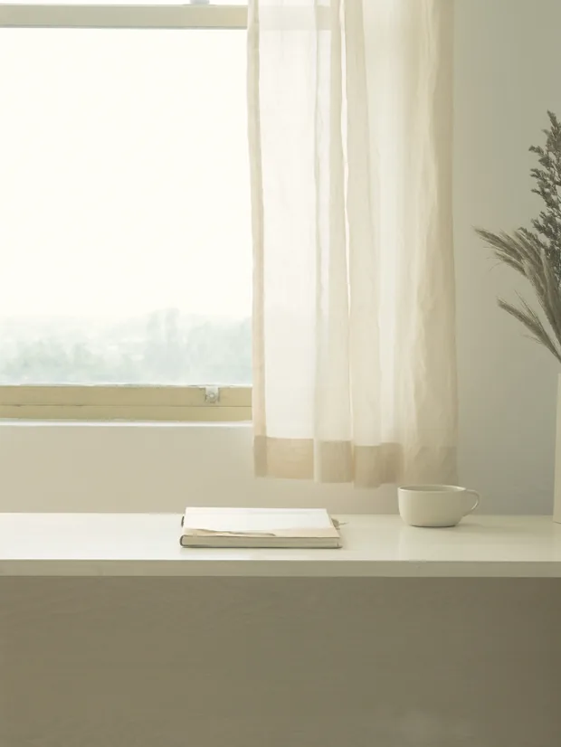 Bright window with a linen curtain, an open notebook and a white cup in front of it