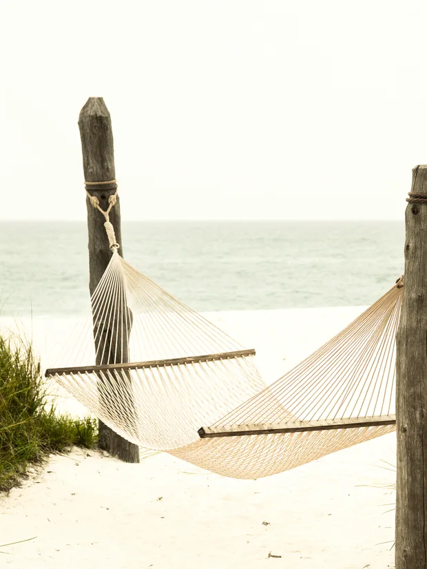 Empty hammock between two wooden posts on bright sand, calm sea behind it