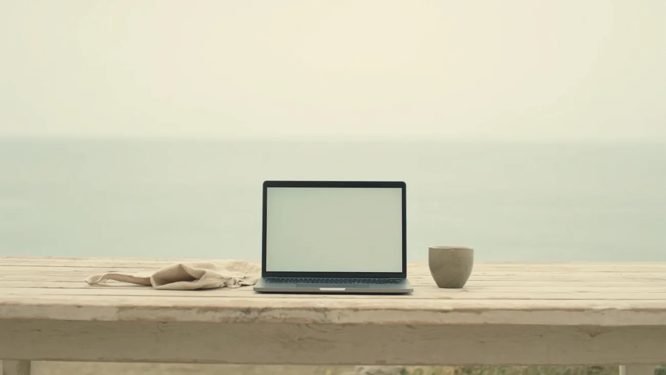 Open laptop on a light wooden table, a calm sea horizon behind it