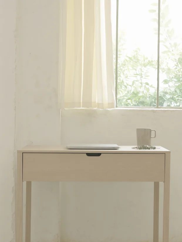 Quiet desk at a bright window with a closed laptop and a cup on it